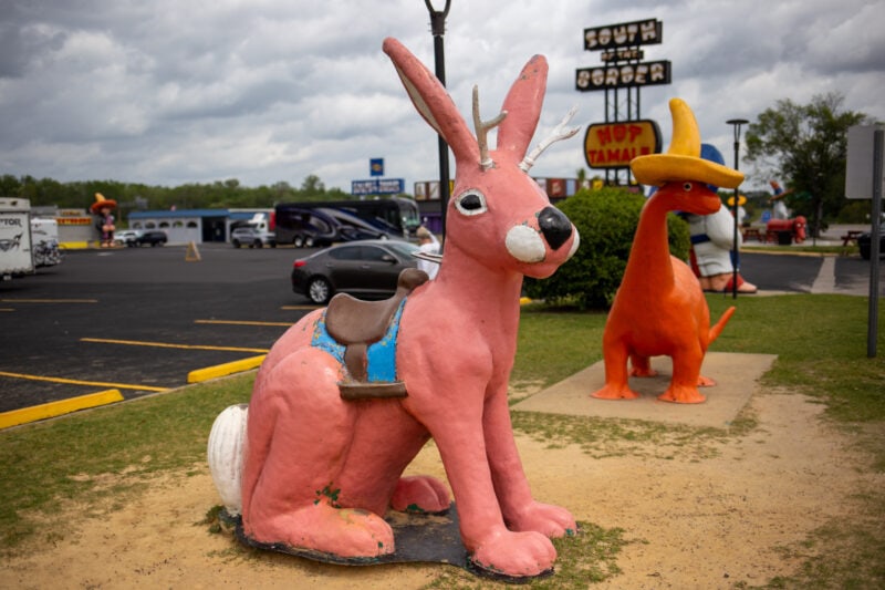 fiberglass statues of a pink jackalope and orange dinosaur wearing a yellow sombrero