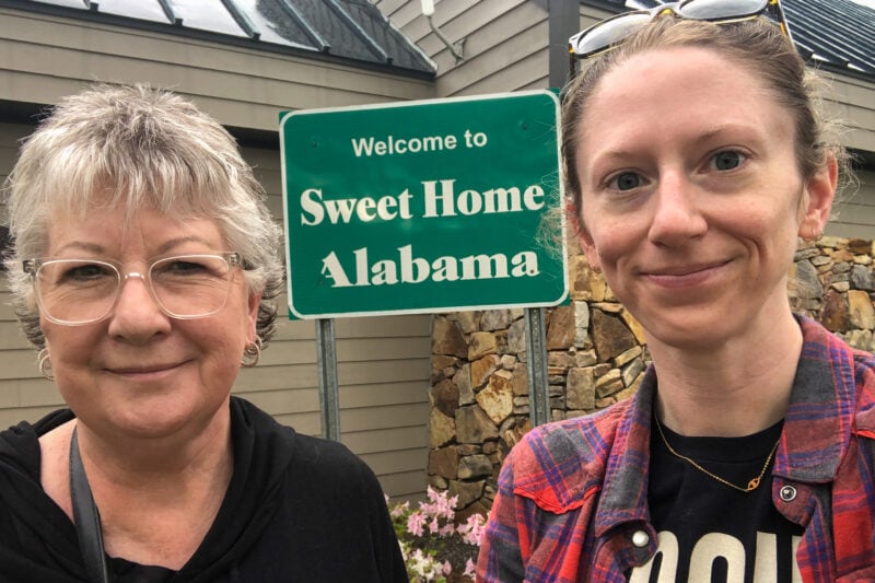 two people take a selfie in front of a green road sign that says "welcome to sweet home alabama"