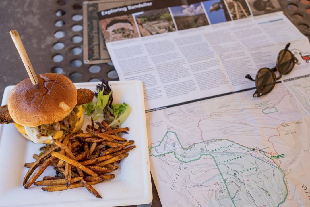 A burger and fries on a platter next to a map, visitor guide, and sunglasses on a table