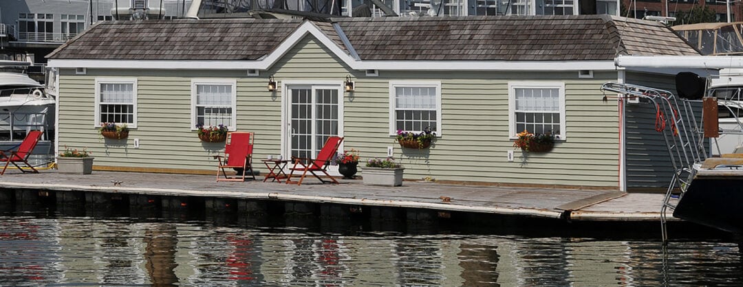 a one-story houseboat with light green siding by the water's edge