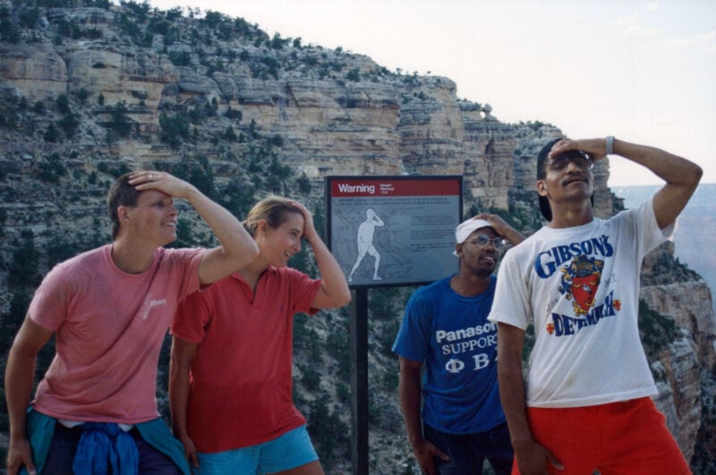 four people with their hands on their head in front of a mountain overlook