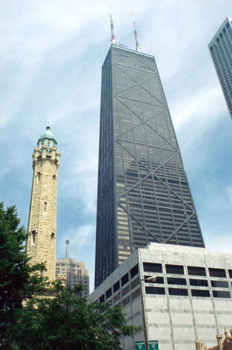 a tall black glass skyscraper next to a tall stone tower in front of a blue sky