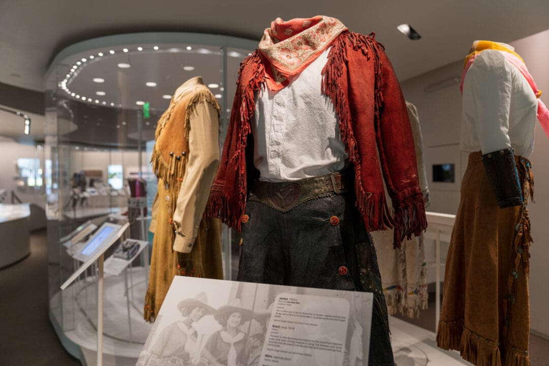 wild west costumes including fringed jackets and neck bandanas on display in a museum