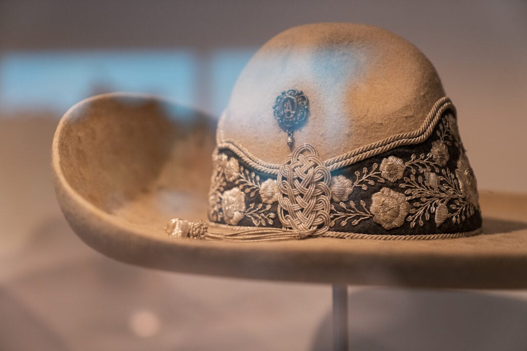a felt beige cowboy hat with an embroidered band on display in a museum case