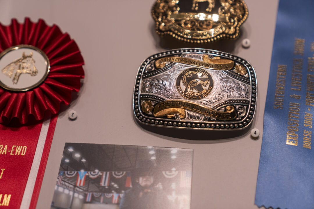 silver and gold belt buckles and show ribbons on display in a museum case
