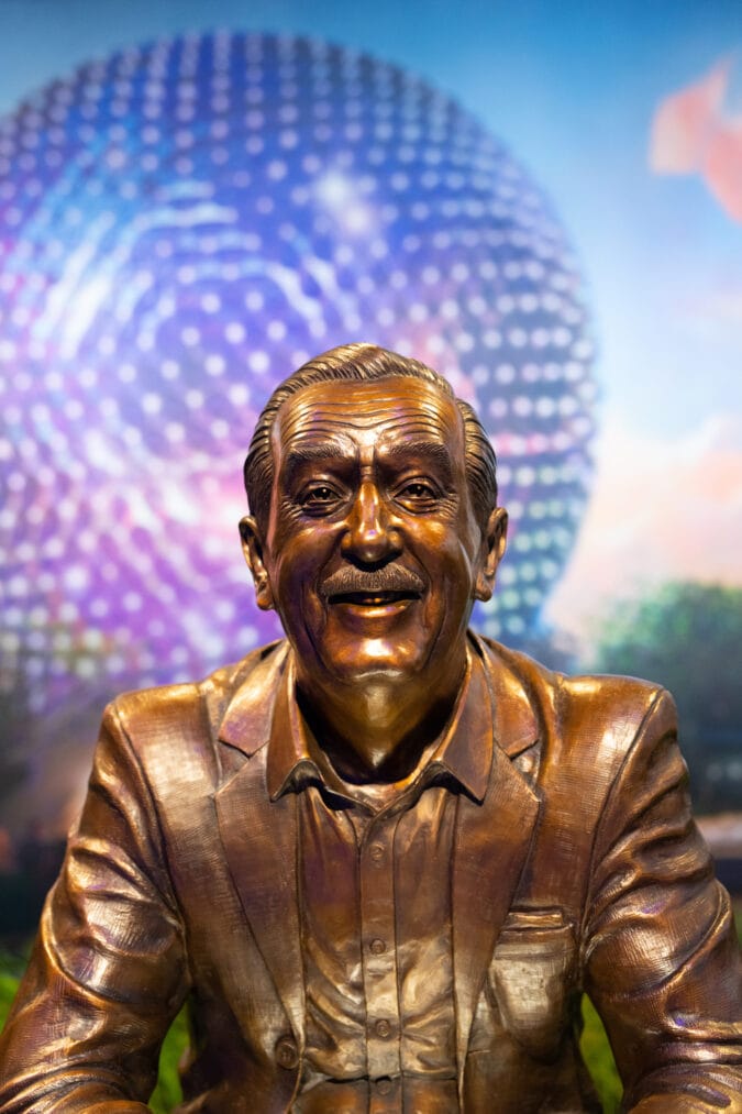 a bronze statue of walt disney in front of epcot's large sphere