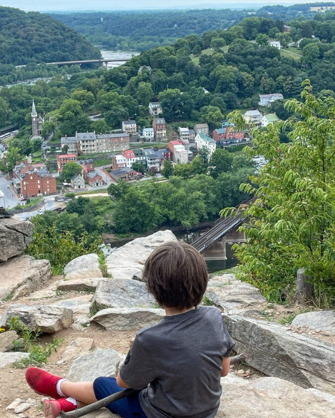 a boy sits on a rock overlooking a valley filled with colorful homes and structures