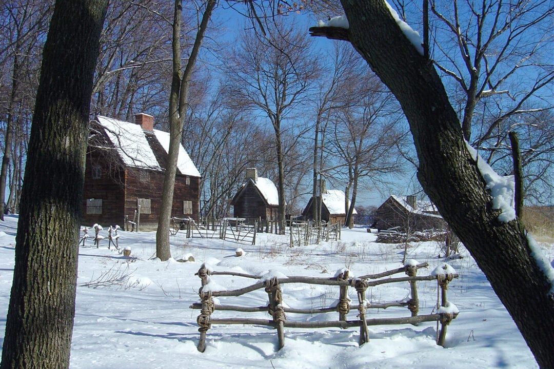 a 1600s pioneer village with wooden cabins in the snow