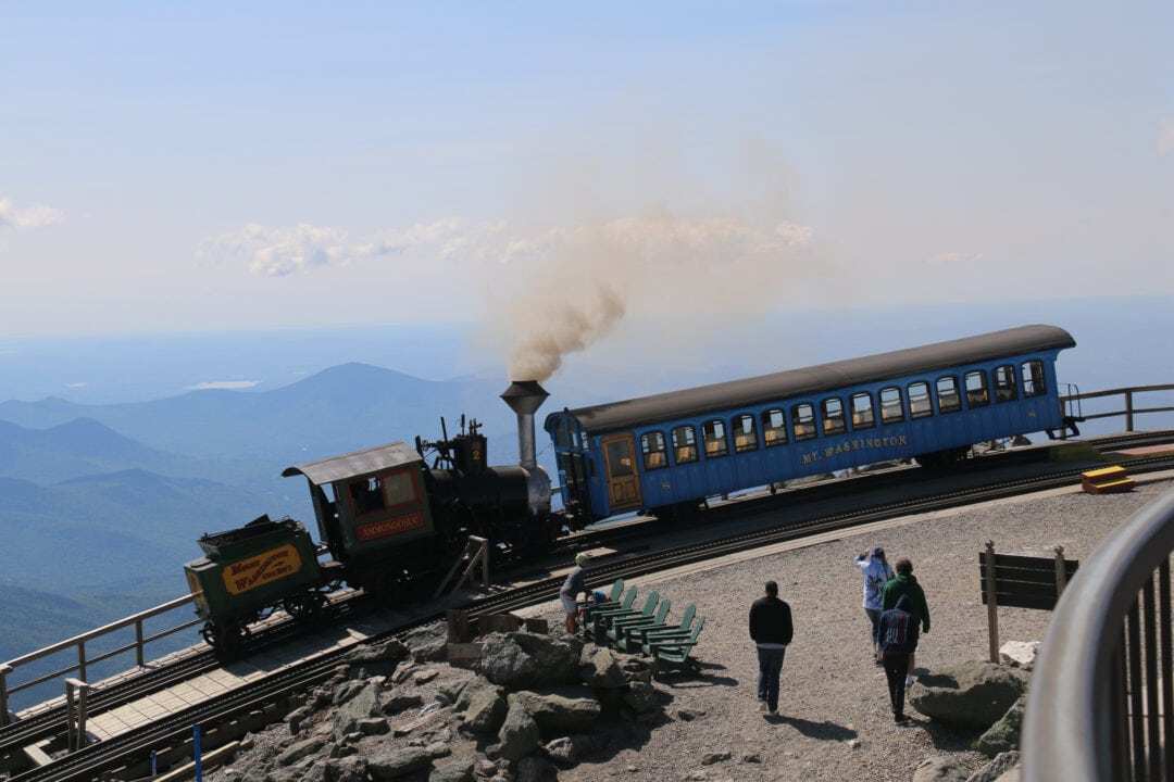 A steam powered train on a track at the summit of a mountain