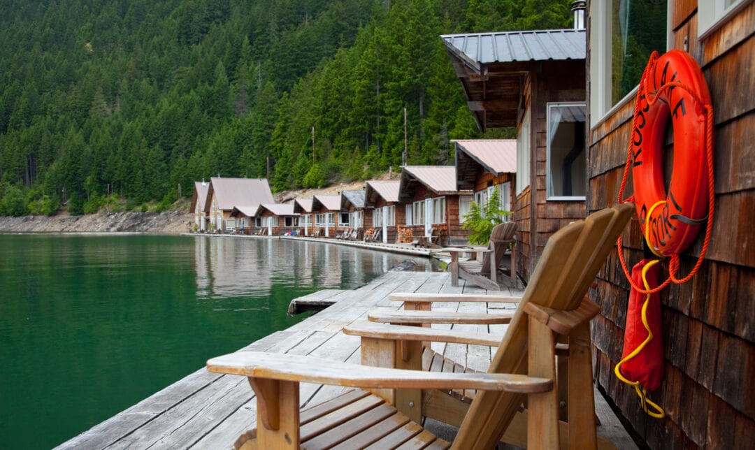 a lake circled by floating wooden cabins with adirondack chairs and life preservers