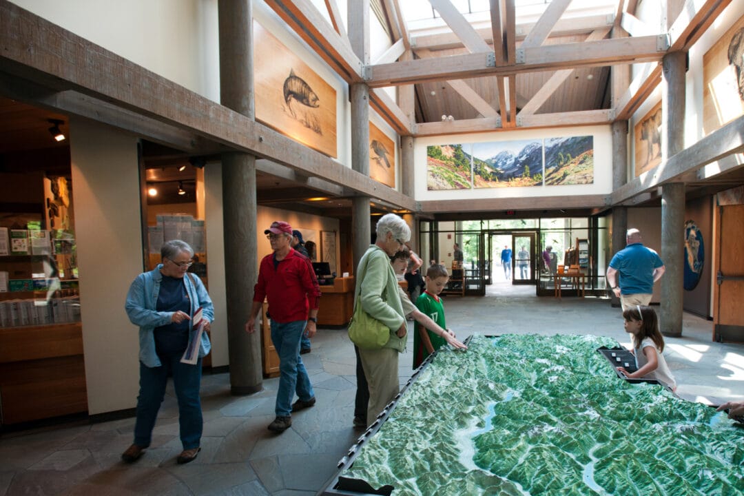 people walk around a visitor center looking at exhibits including a large topographic map