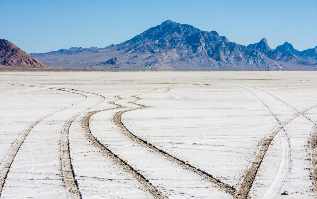 Tire tracks through a salt flats with mountains in the distance