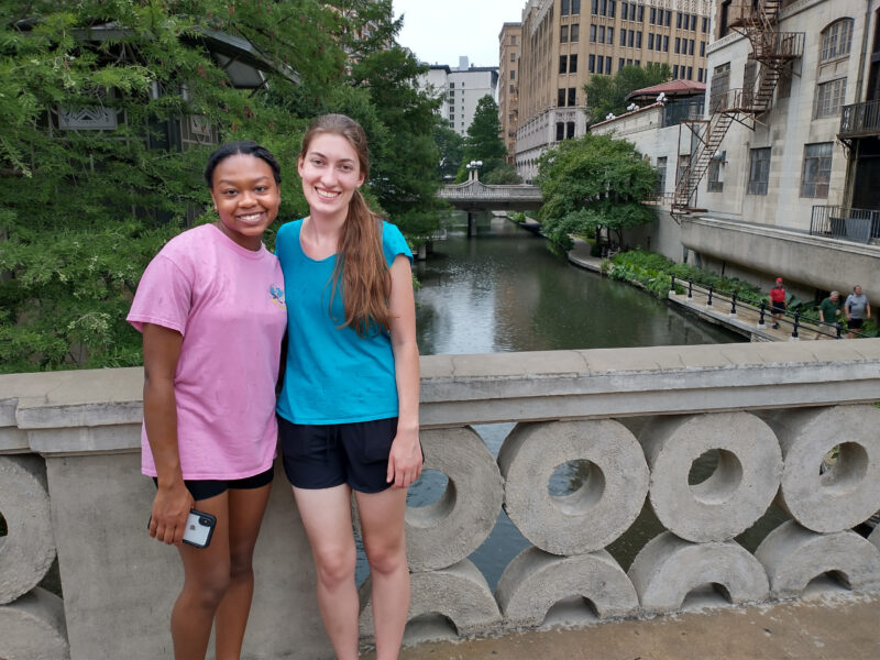 two people stand on a concrete bridge over a waterway in a city