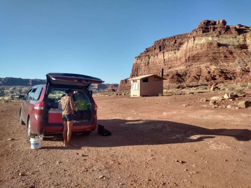 a person stands by the open back hatch of a red minivan parked in the desert