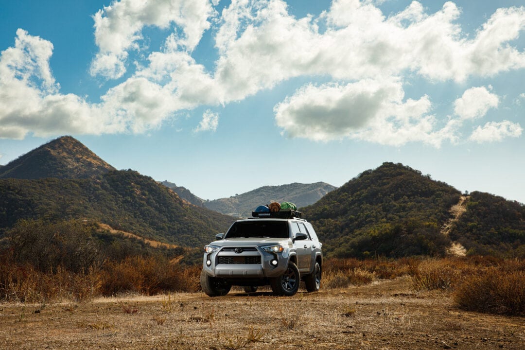 a silver suv parked outside near mountains under a blue sky with fluffy white clouds