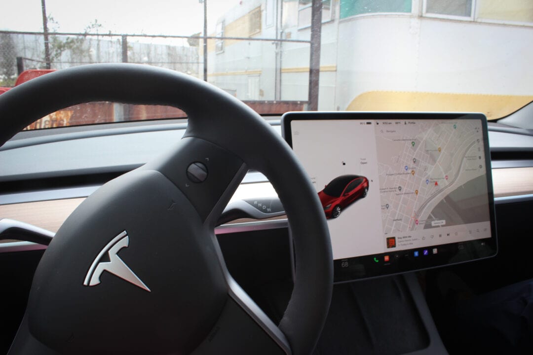 Steering wheel and large electronic screen showing a car simulation and map inside an EV