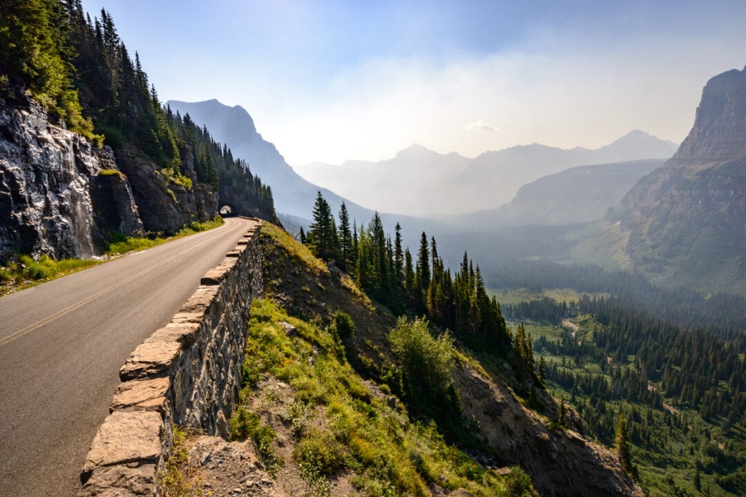 A scenic road winds its way through stunning view of mountains and towering trees.