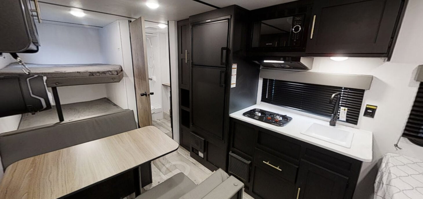 Interior view of small travel trailer with kitchen, dinette, and bunks; door is ajar to bathroom