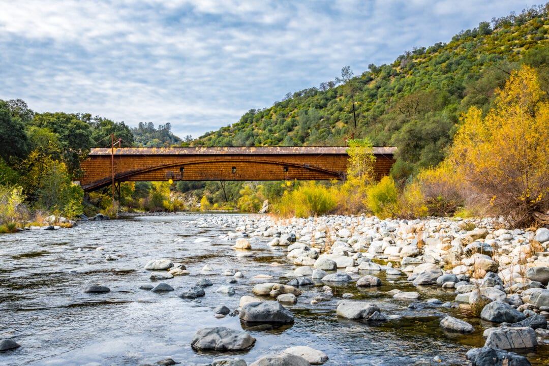 A covered bridge spans across a rocky river.