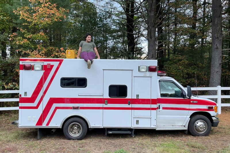 a person sits on top of white ambulance with red stripes