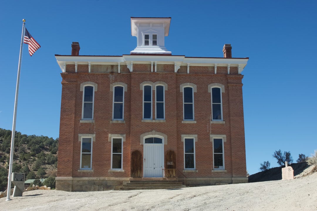a two story brick courthouse in the desert set against a clear blue sky with a flag pole out front and a small white cupola