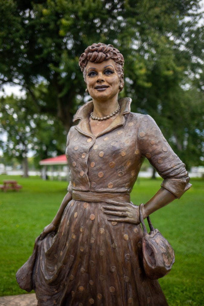 a bronze statue of lucille ball wearing a polka dot dress and holding a purse