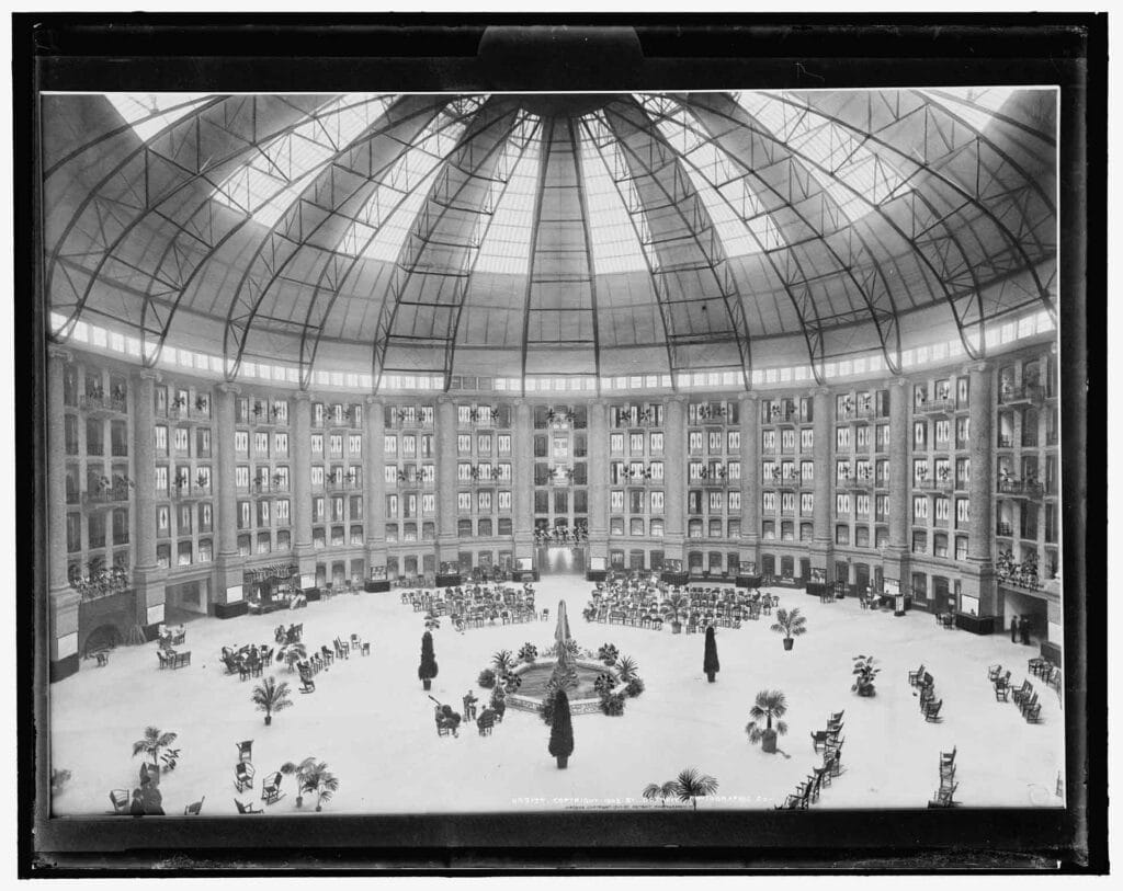 a black and white photo of a grand circular hotel atrium with plants, chairs, and a large dome