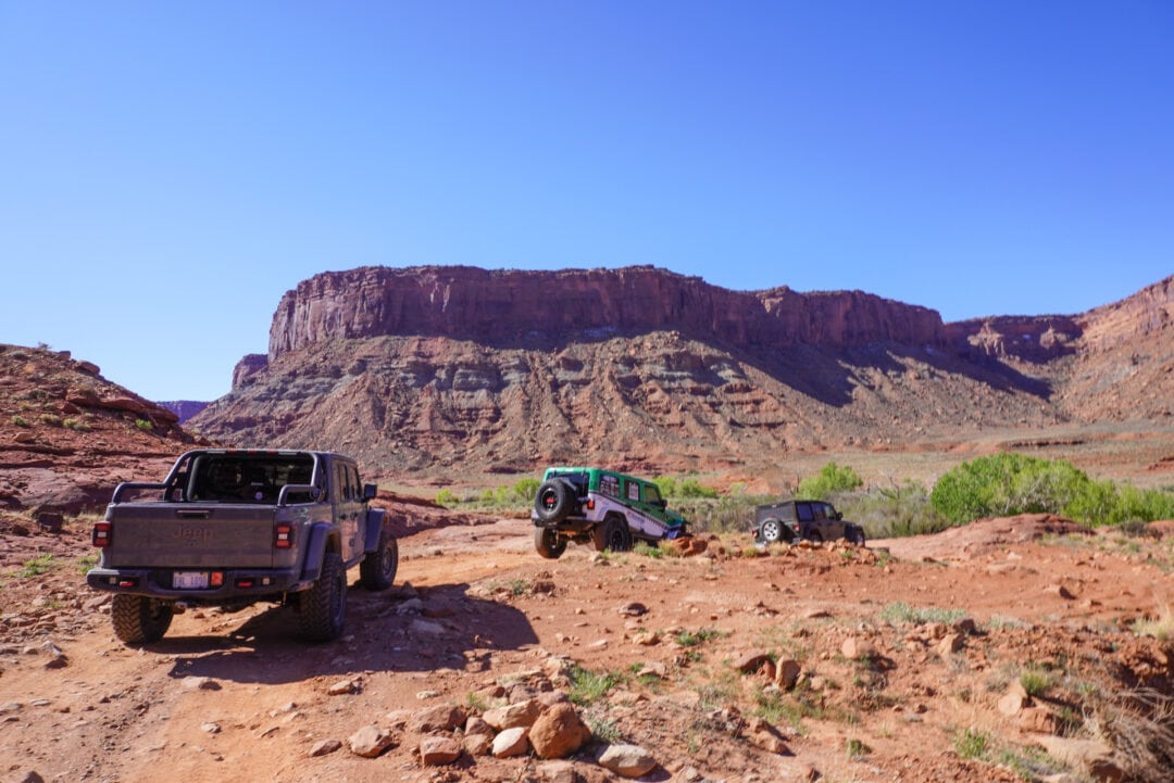 A row of Jeeps traveling in a red-rock desert landscape