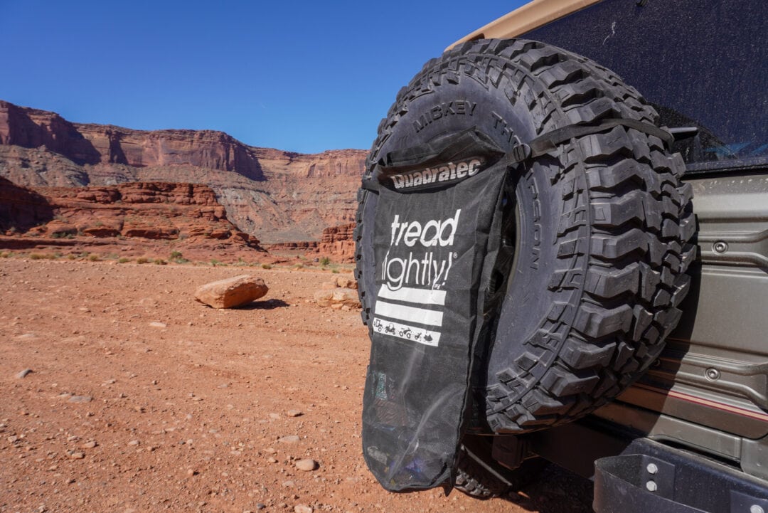 Close-up of a Tread Lightly trash bag hanging on the spare tire of a Jeep, with desert red rocks in the background