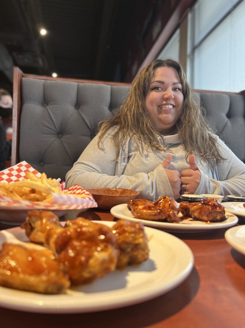 a person gives the thumbs up sitting in a restaurant booth with a plate of chicken wings