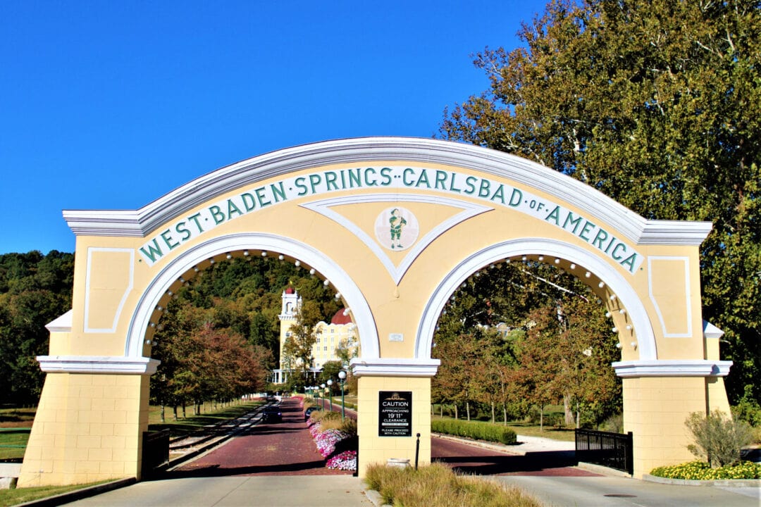 a double arching yellow and white gate that says "west baden springs carlsbad of america"