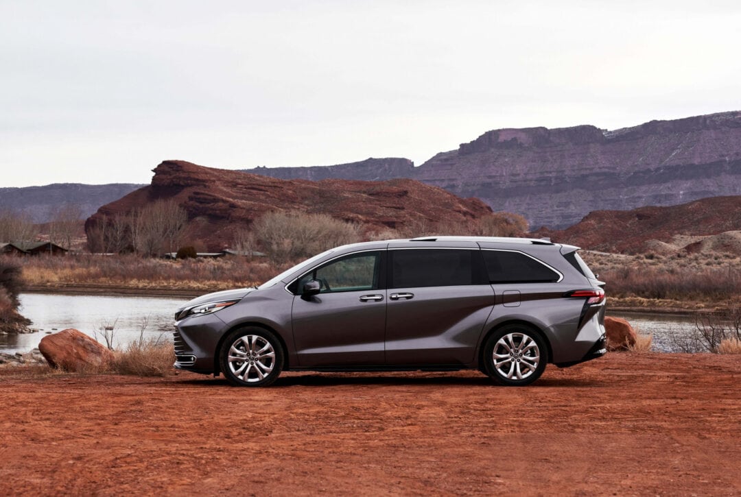 A minivan is parked on a dirt road alongside red rock formations.