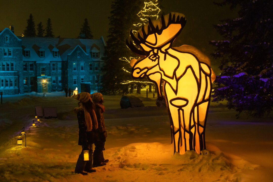 On a dark night, children look in awe at a huge lighted sculpture of a moose.