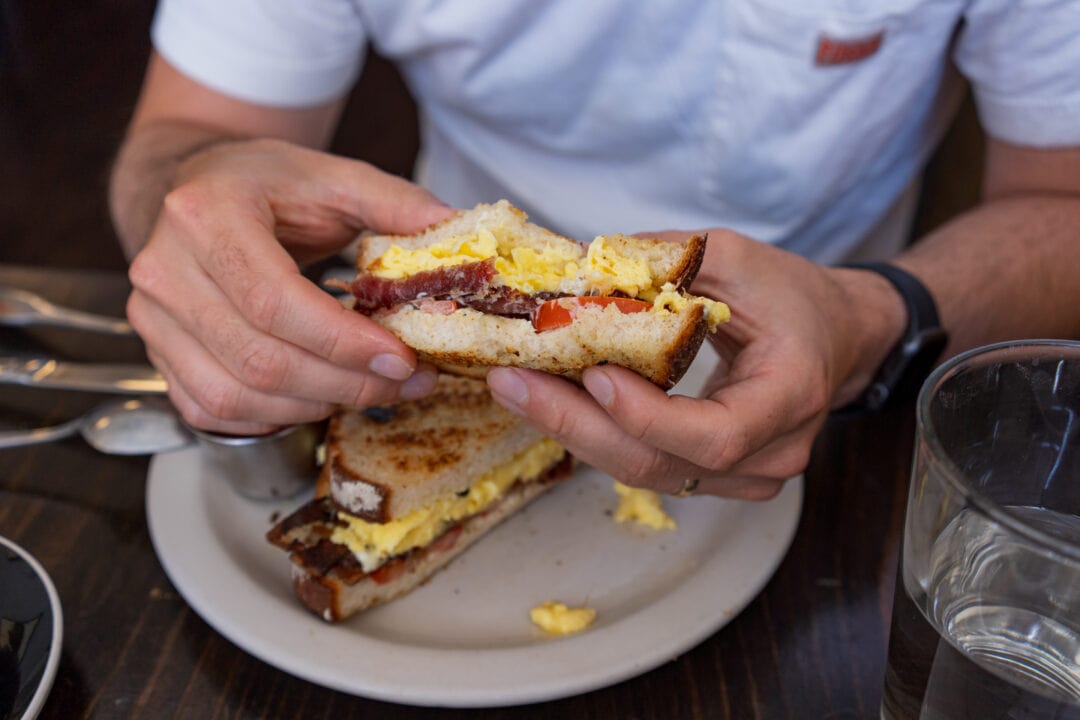 A breakfast sandwich is stuffed with scrambled eggs, meat, and tomatoes.