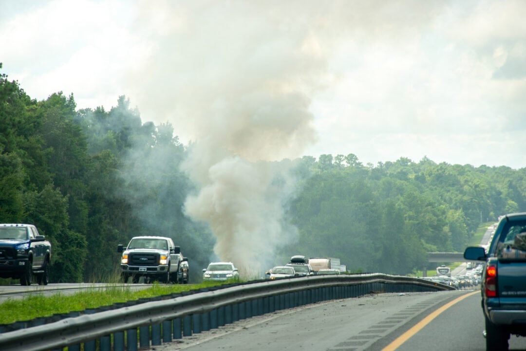 Smoke billows from a car stranded on a busy roadway.