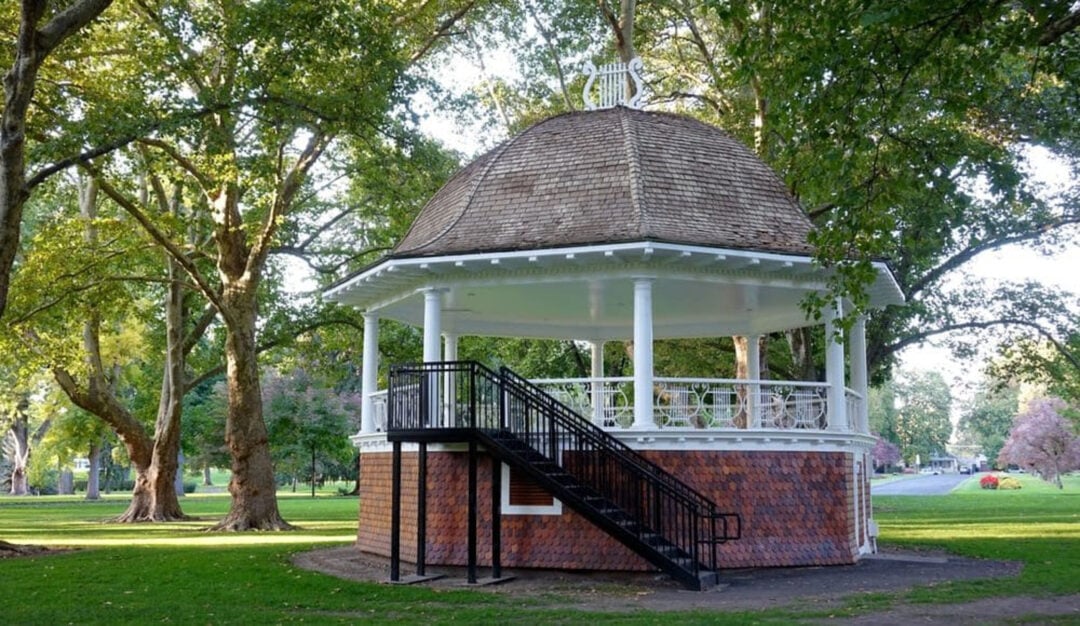 A sizeable and attractive gazebo located in a tree-lined park.
