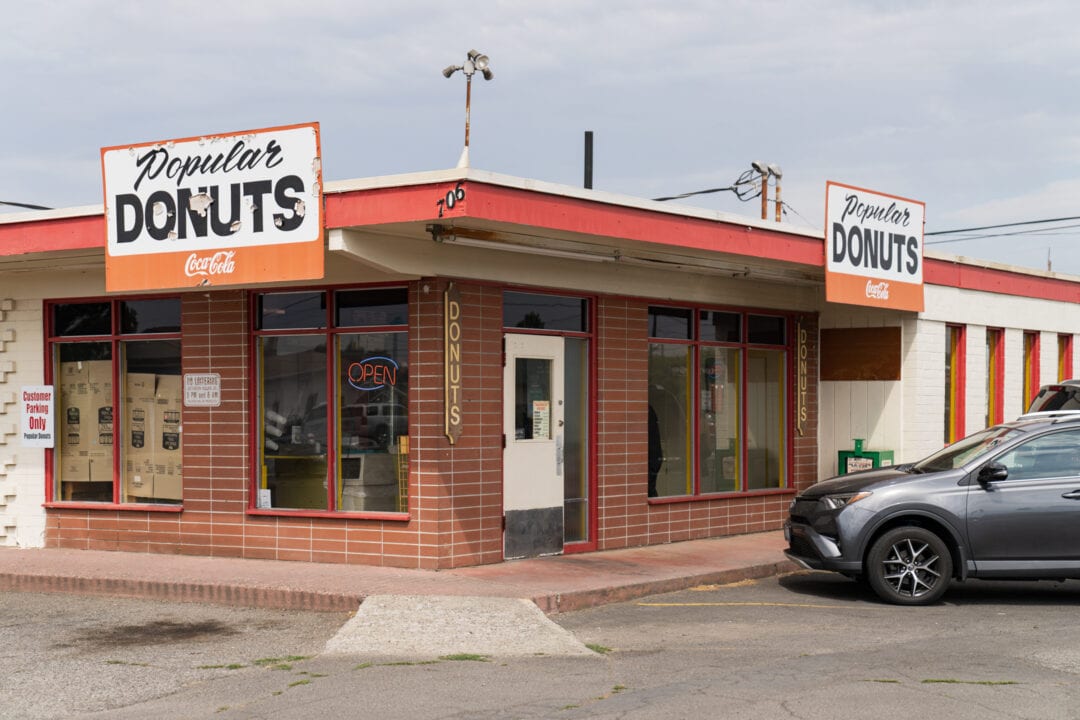 A small, well-established donut shop stands at the end of a strip mall.