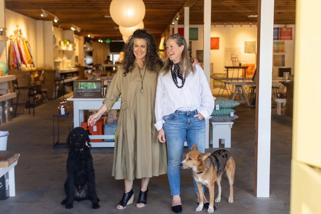Two women and their dogs stand at the entrance of a boutique store.