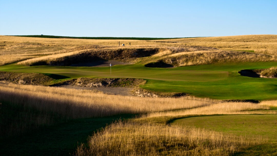 A hole on a golf course offers water and sand traps lining the green.