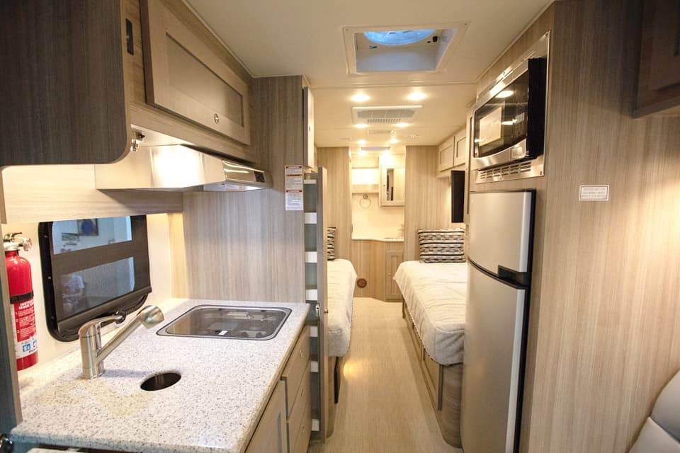 The interior of a small motorhome showing sink, fridge, two beds, and bathroom in the rear