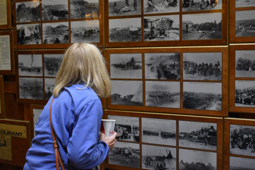 A woman looks through black and white photos lining a wooden wall.