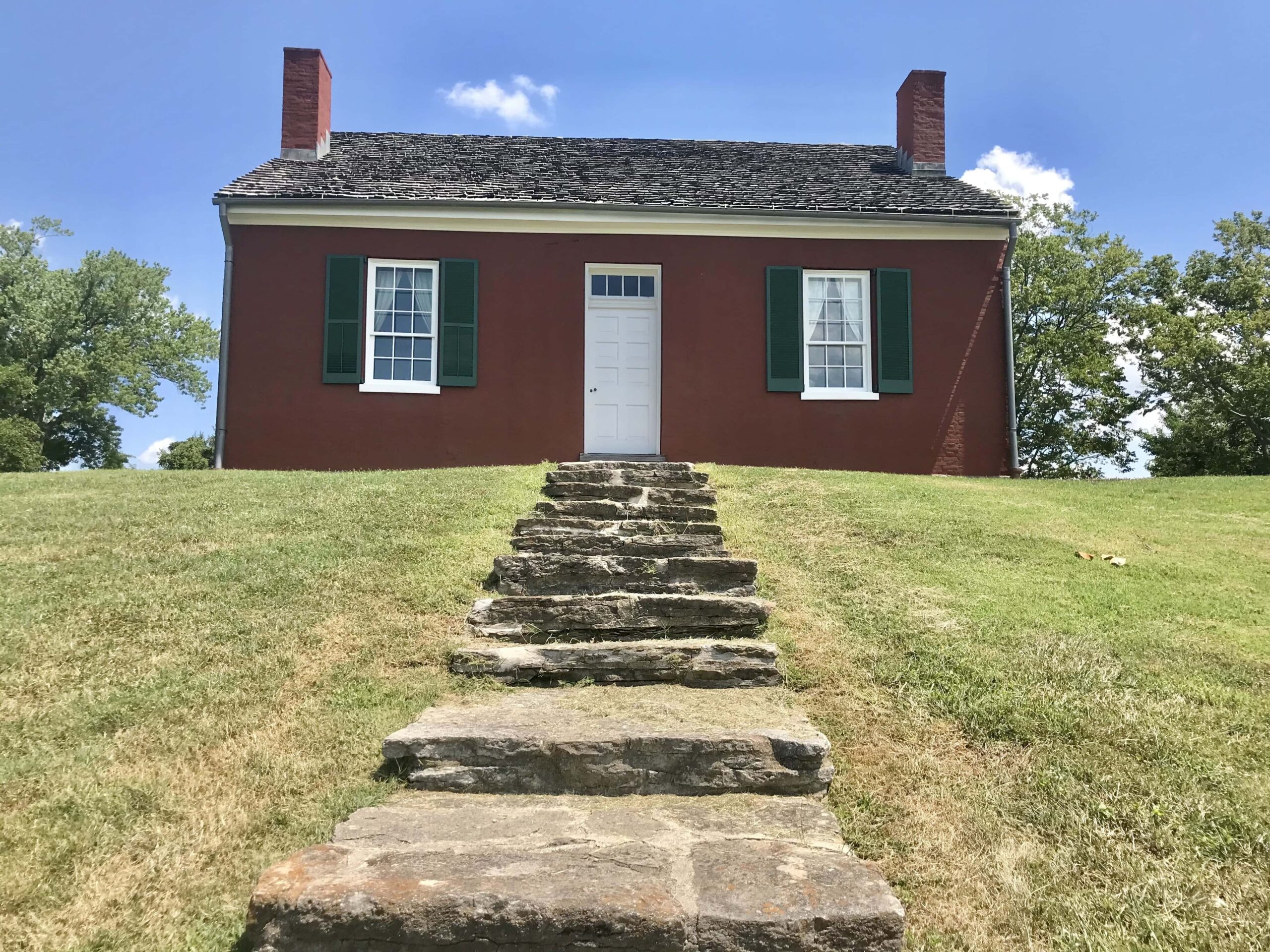 Rough stone slab steps lead up a grassy hill to a small house.