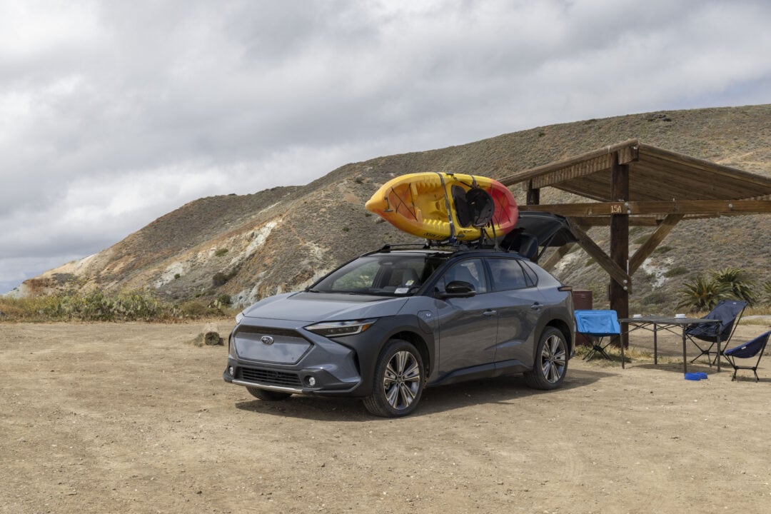 A small car is loaded up with outdoor gear, including a prominent kayak on the roof rack.