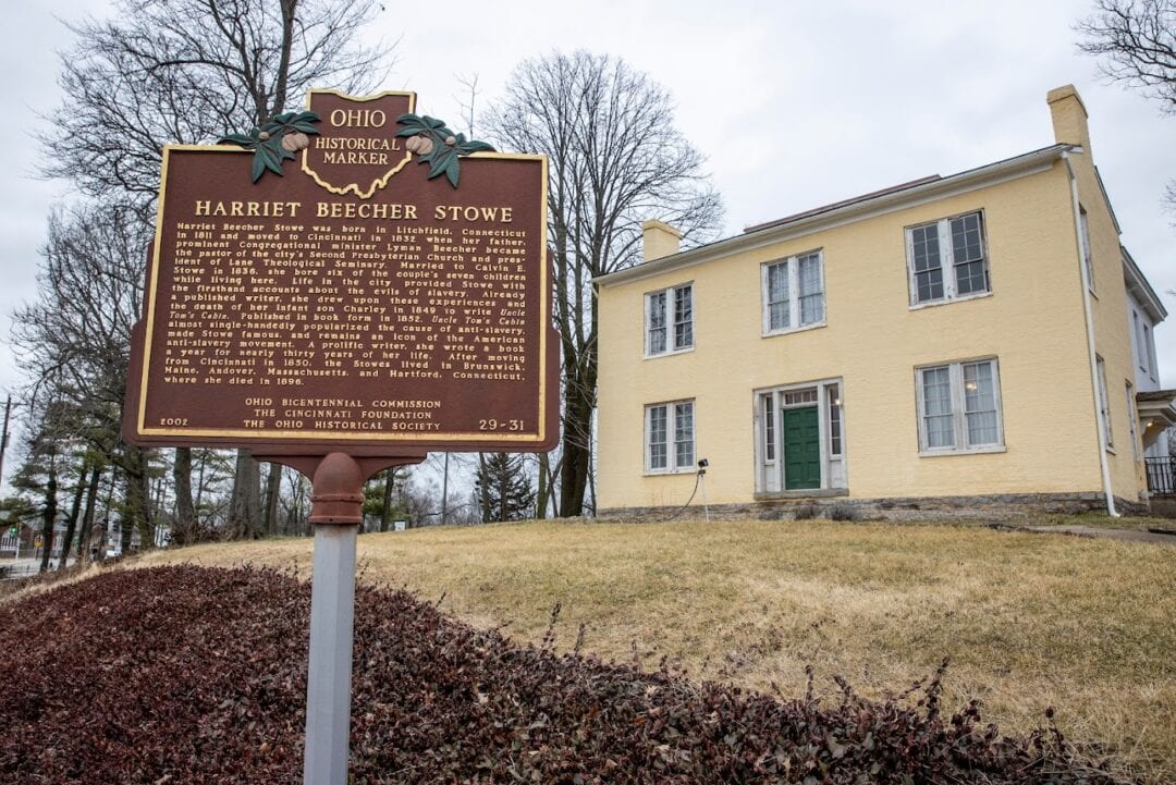 A historical marker stands in front of a small two-story house.