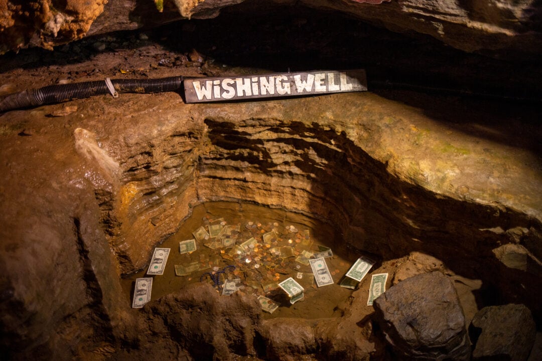 a handpainted wooden sign that says "wishing well" inside a cave with a rocky pond with money in it
