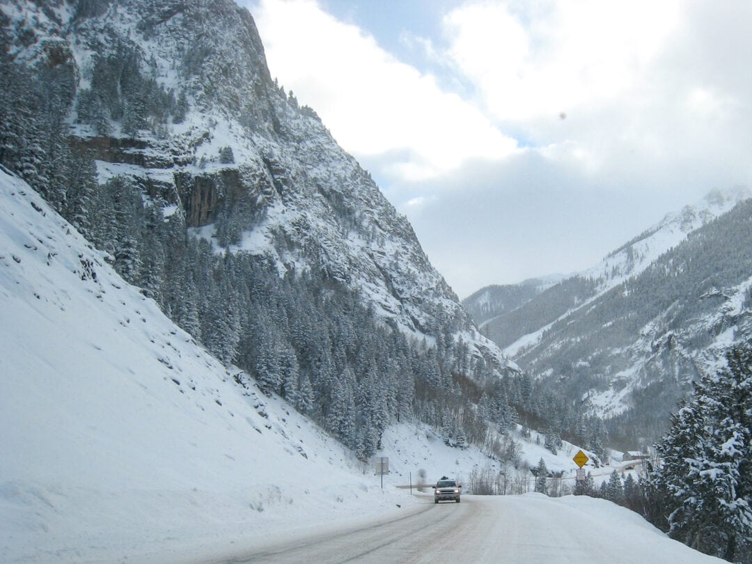 Fresh snow covers a road surrounded by steep mountain cliffs.