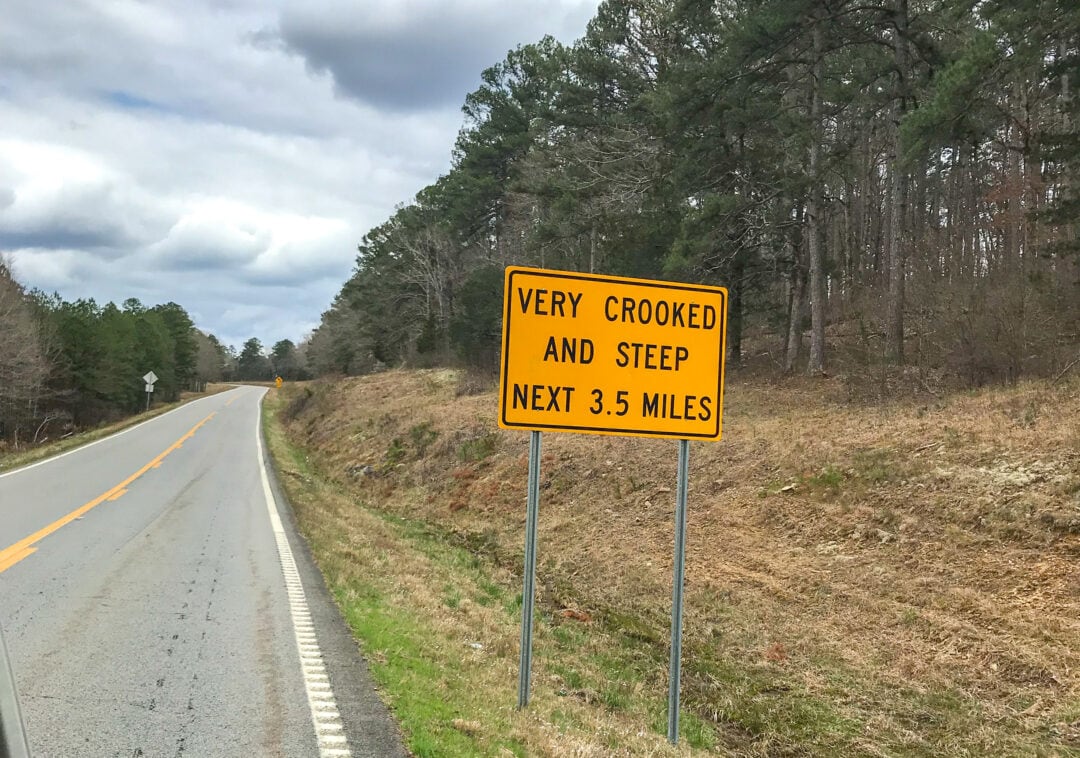 A roadside caution signs reads "Very crooked and steep next 3.5 miles."