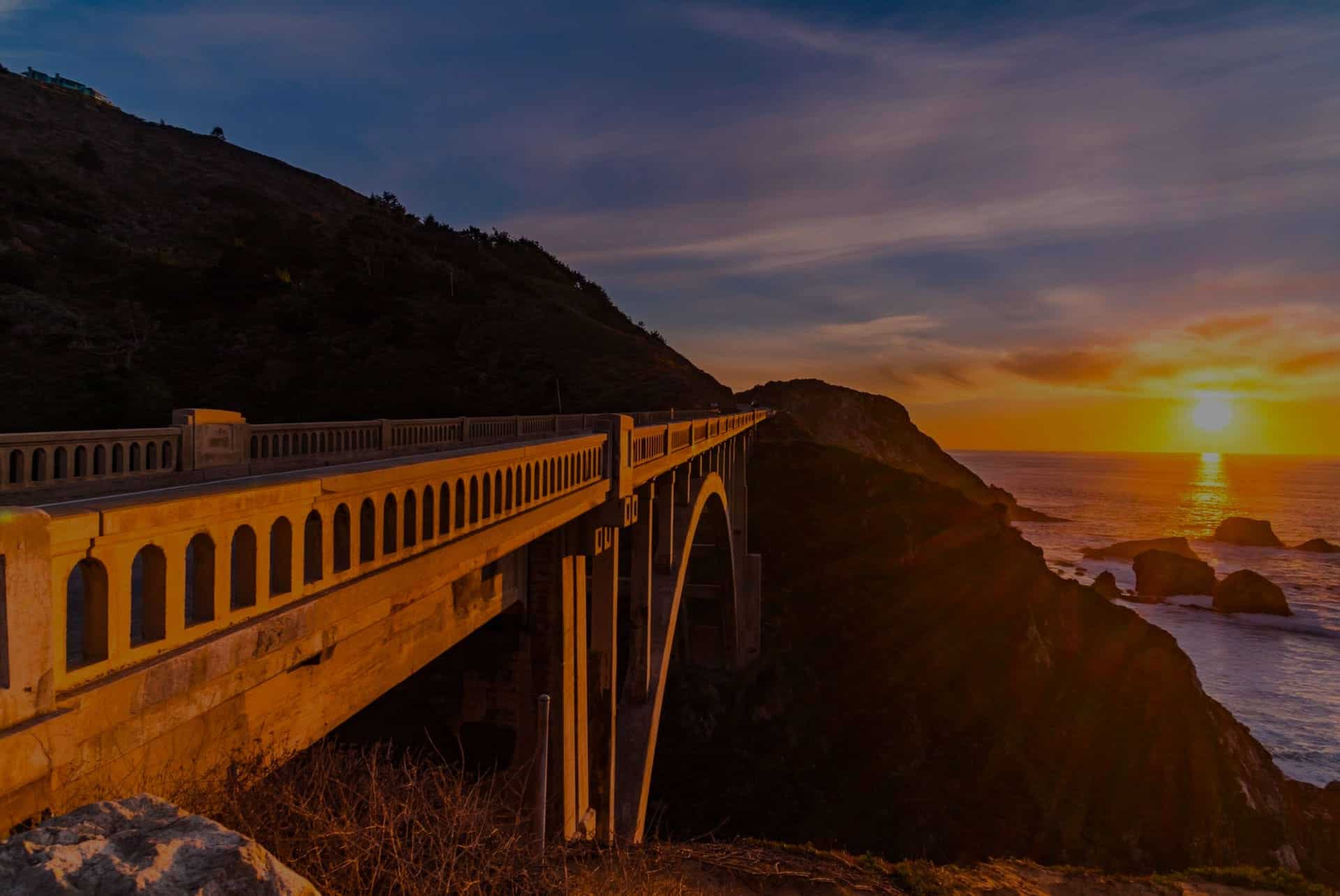 A bridge next to the ocean during sunset