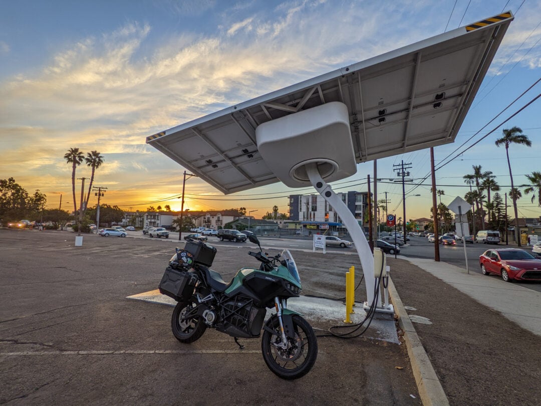 A motorcycle parked at an EV charging station at sunset