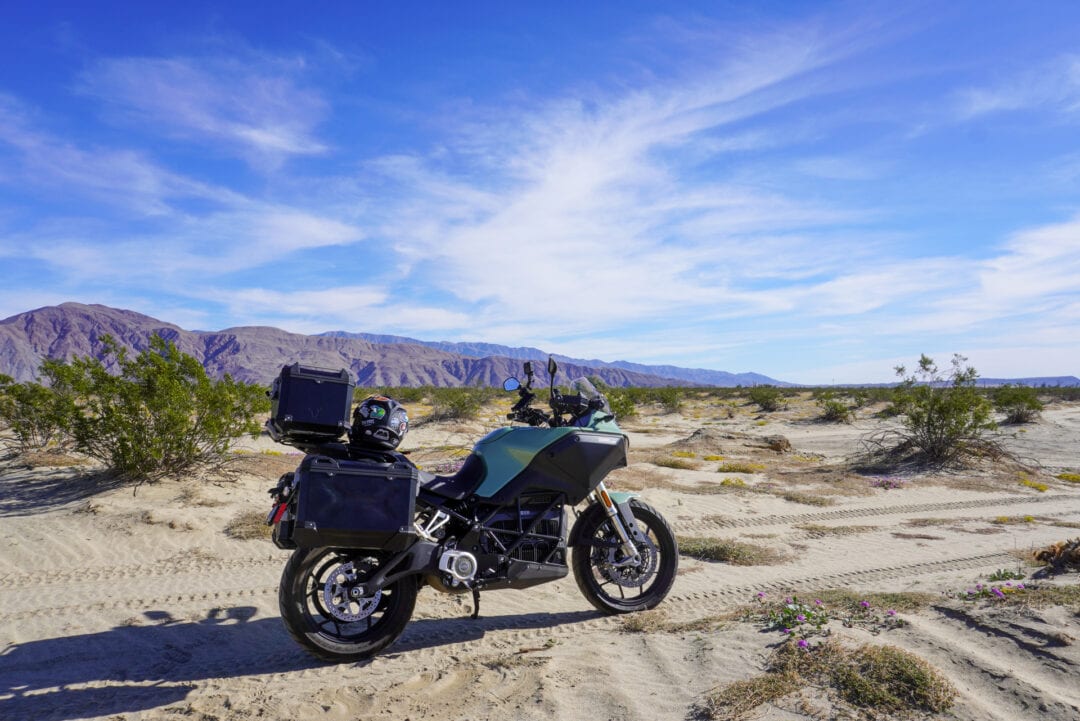 A green and black adventure motorcycle parked in a desert landscape
